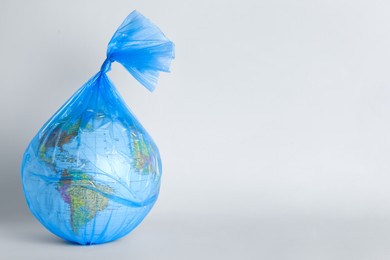 Photo of Globe in plastic bag on light background, space for text. Environmental conservation