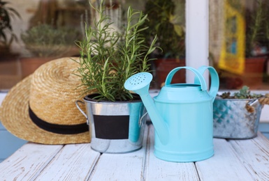 Photo of Potted plant, watering can and straw hat on white wooden table near window. Gardening tools