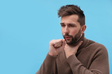 Photo of Man coughing on light blue background, space for text. Cold symptoms