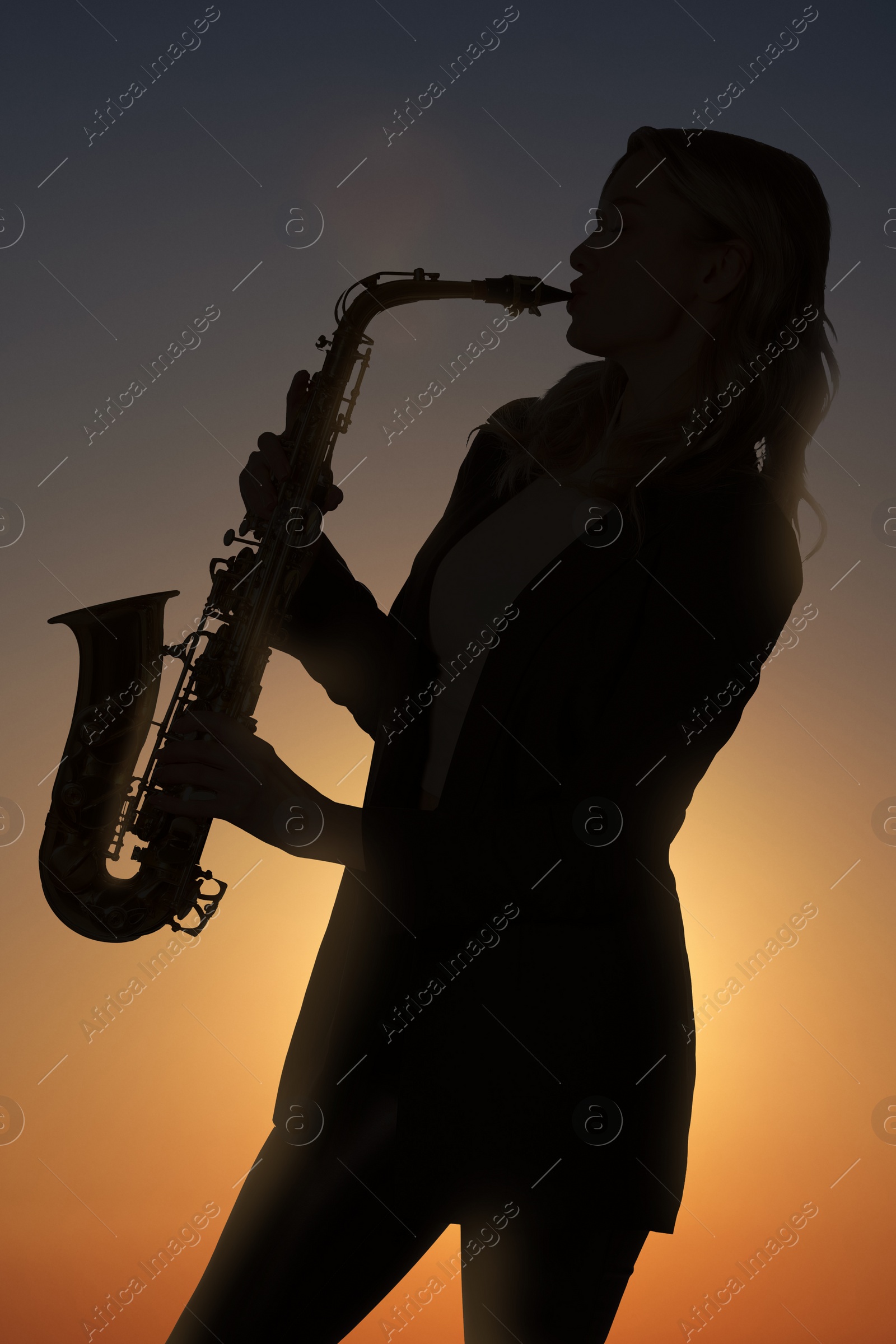 Image of Silhouette of woman playing saxophone against beautiful sky at sunset