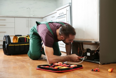 Male technician in uniform repairing refrigerator indoors