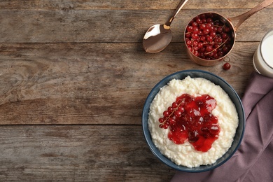 Photo of Creamy rice pudding with red currant and jam in bowl served on wooden table, top view. Space for text