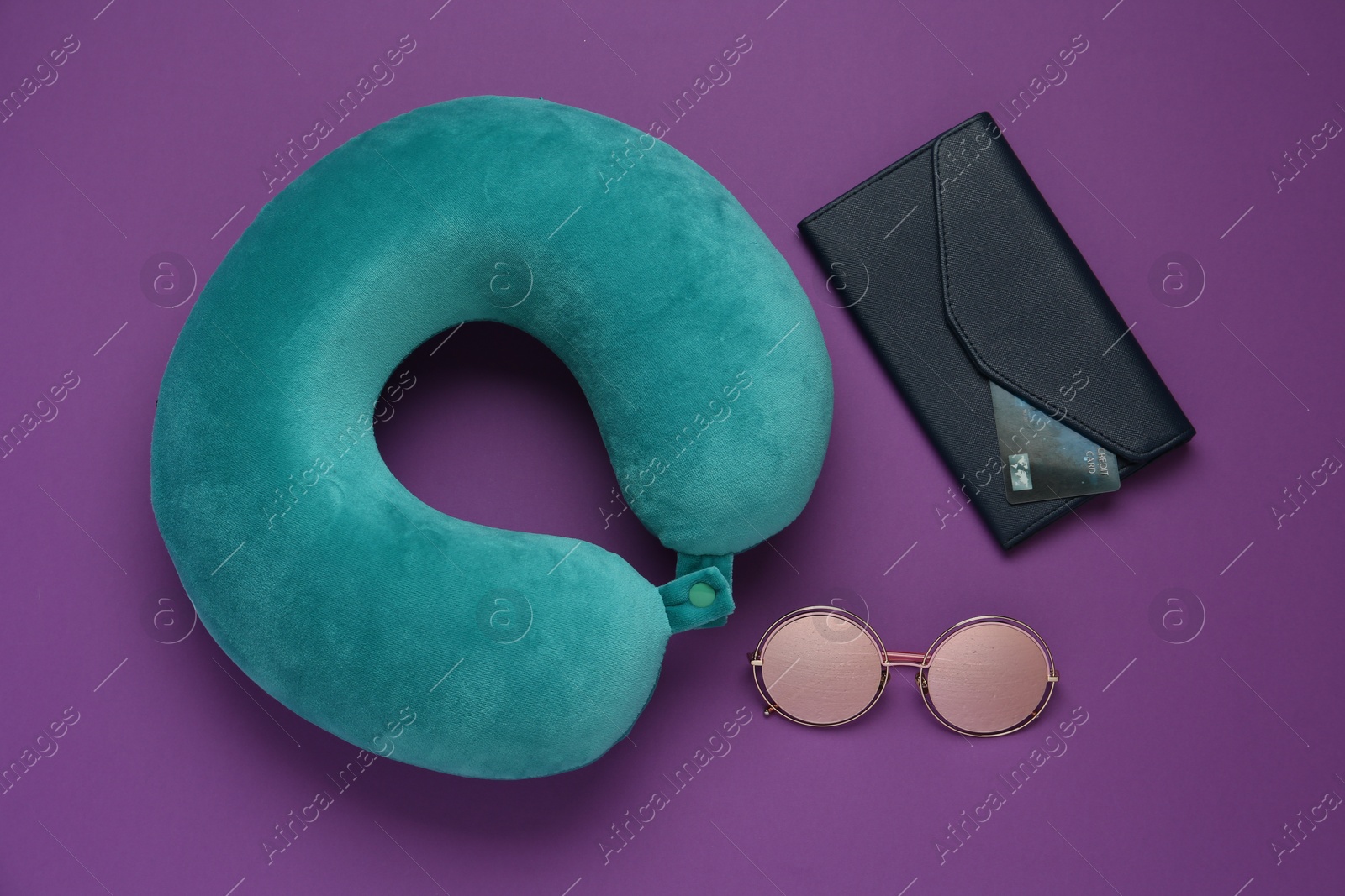 Photo of Turquoise travel pillow, wallet with credit card and sunglasses on purple background, flat lay