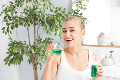 Photo of Woman holding bottle and glass with mouthwash in bathroom. Teeth care