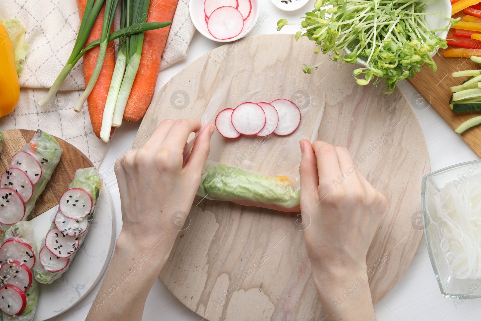 Photo of Woman wrapping spring roll at white wooden table with products, top view