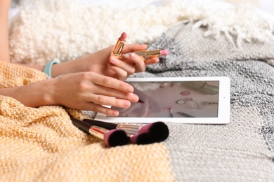 Photo of Young woman with makeup products using tablet on bed. Beauty blogger