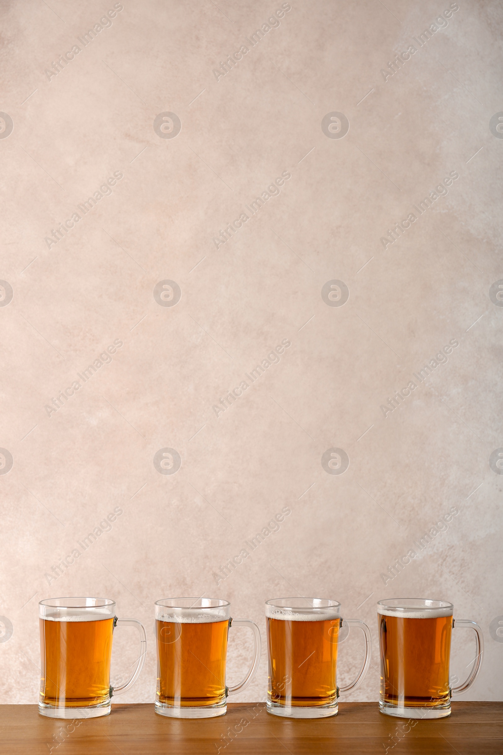 Photo of Glass mugs with beer on table against color background