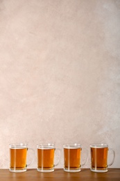 Glass mugs with beer on table against color background