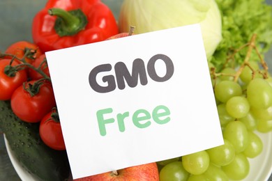 Photo of Fresh fruits, vegetables and card with text GMO Free on table, closeup