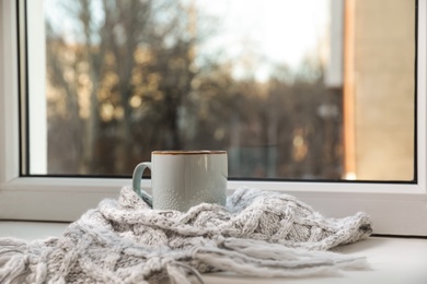 Cup of winter drink and knitted scarf on windowsill. Space for text