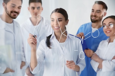 Medical students writing chemical formula on glass whiteboard in laboratory