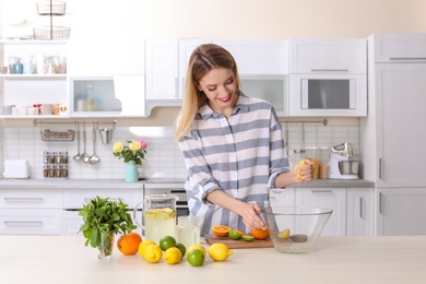 Photo of Young woman squeezing juice into bowl for lemonade on table in kitchen. Natural detox drink
