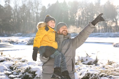 Photo of Happy father pointing at something to his son in sunny snowy park