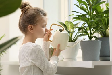 Photo of Cute little girl watering beautiful green plant on windowsill at home. House decor
