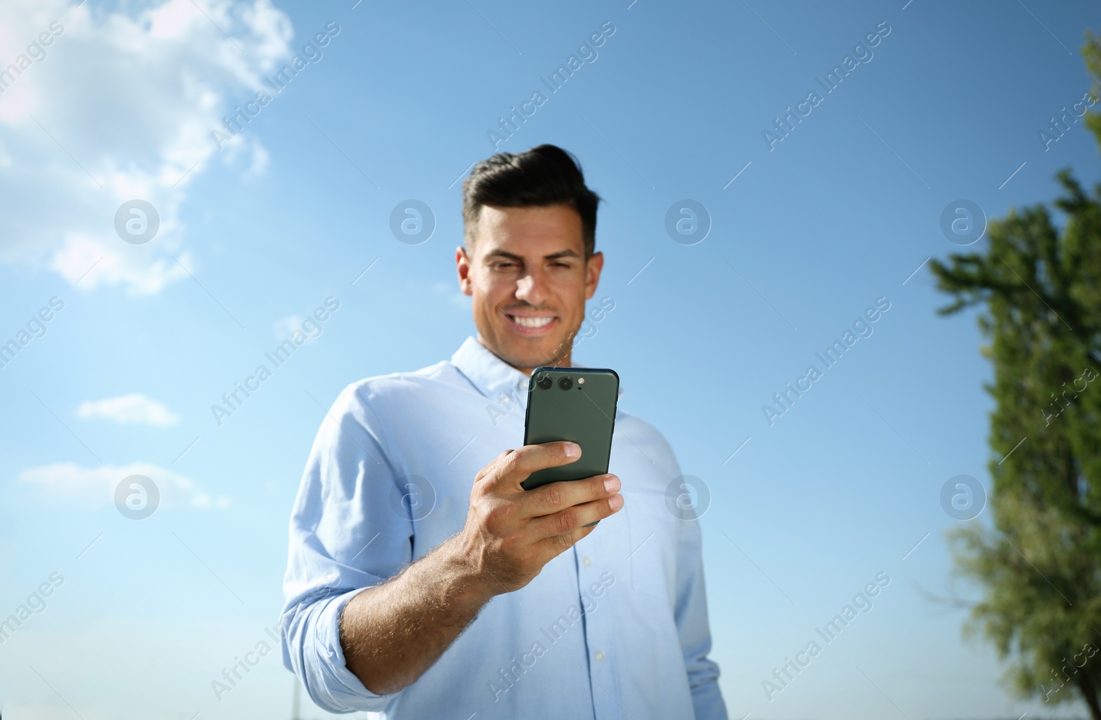 Photo of Handsome man using modern mobile phone outdoors, focus on hand