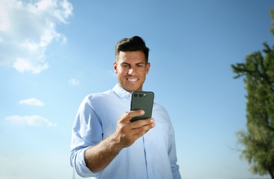 Photo of Handsome man using modern mobile phone outdoors, focus on hand