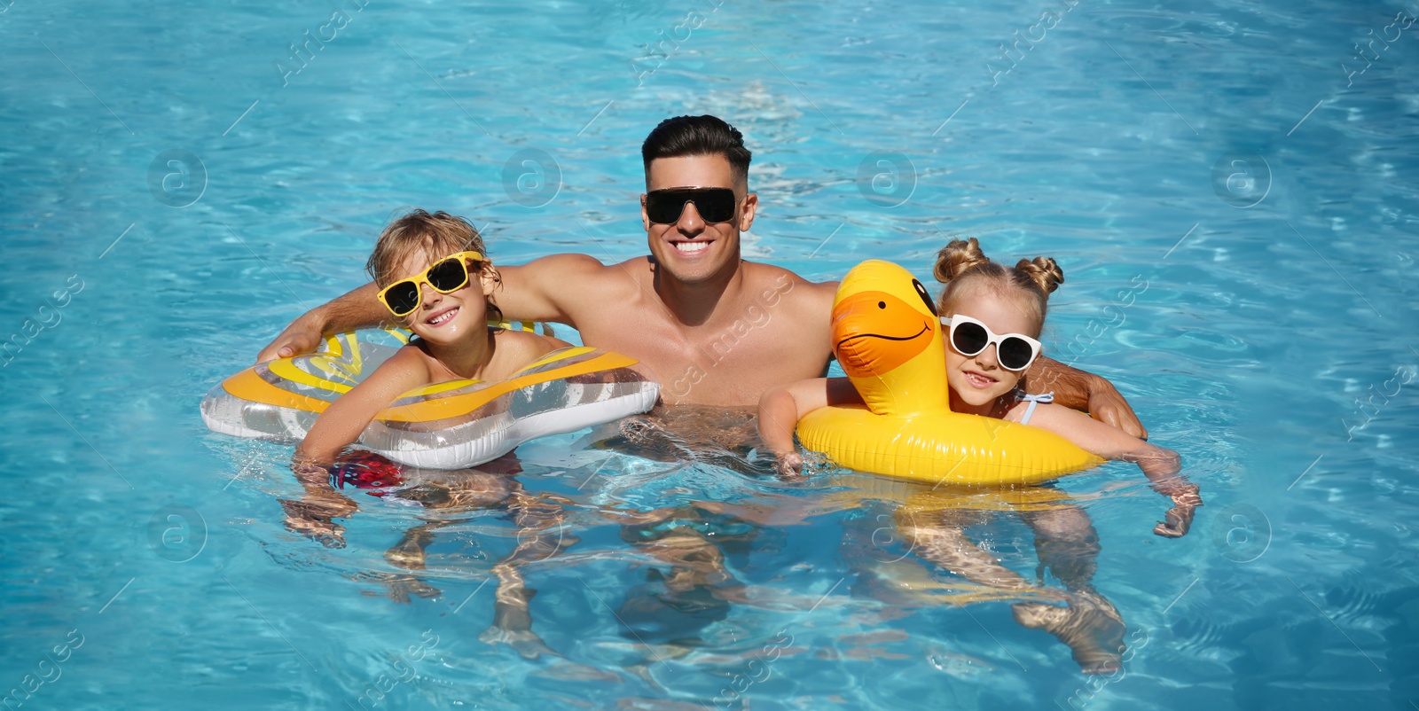 Photo of Happy man and his children with inflatable rings in outdoor swimming pool on sunny summer day