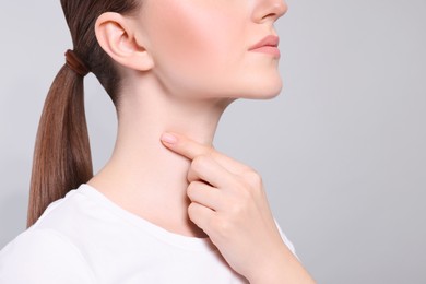 Woman with sore throat on light grey background, closeup