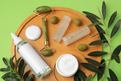 Photo of Different cosmetic products, face roller and olives on light green background, flat lay