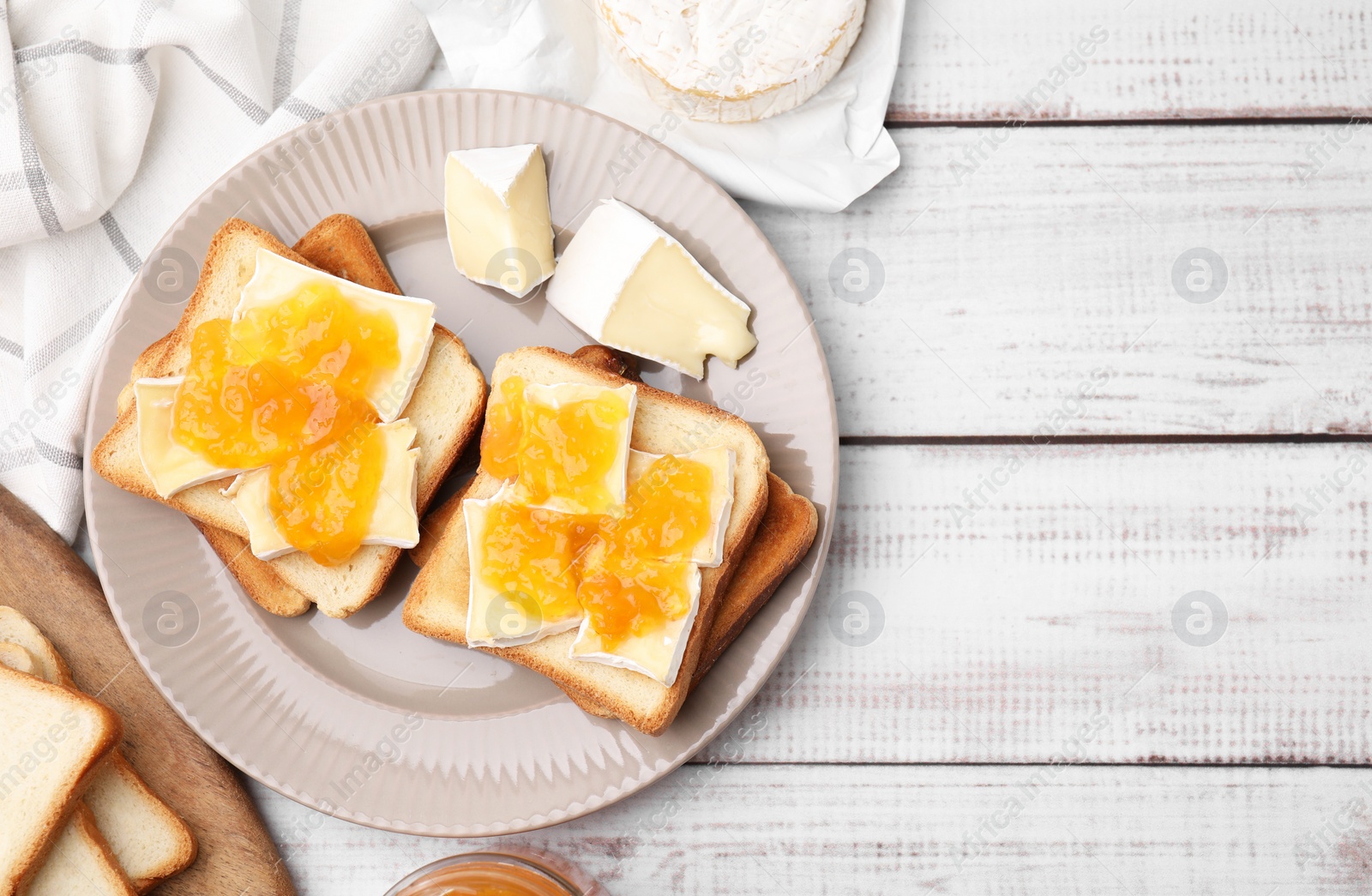 Photo of Tasty sandwiches with brie cheese and apricot jam on white wooden table, flat lay. Space for text