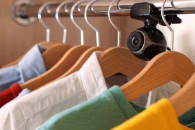 Photo of Camera hidden between hangers in wardrobe closet, closeup