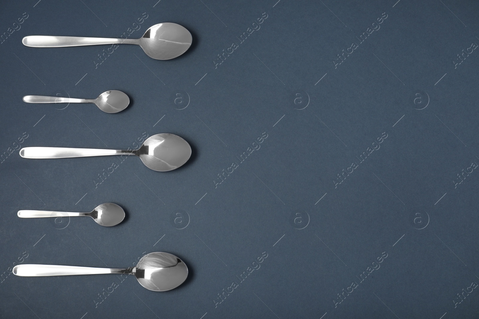 Photo of Set of different spoons on black background, flat lay with space for text