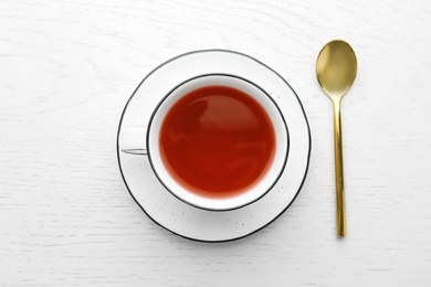 Photo of Cup of hibiscus tea with saucer and spoon on white wooden background, flat lay