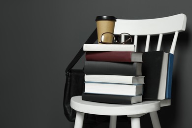Stack of different books, paper cup and glasses on white chair. Space for text