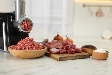 Photo of Electric meat grinder with beef and products on white marble table in kitchen