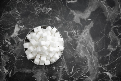 Bowl with refined sugar cubes on dark grey background, top view