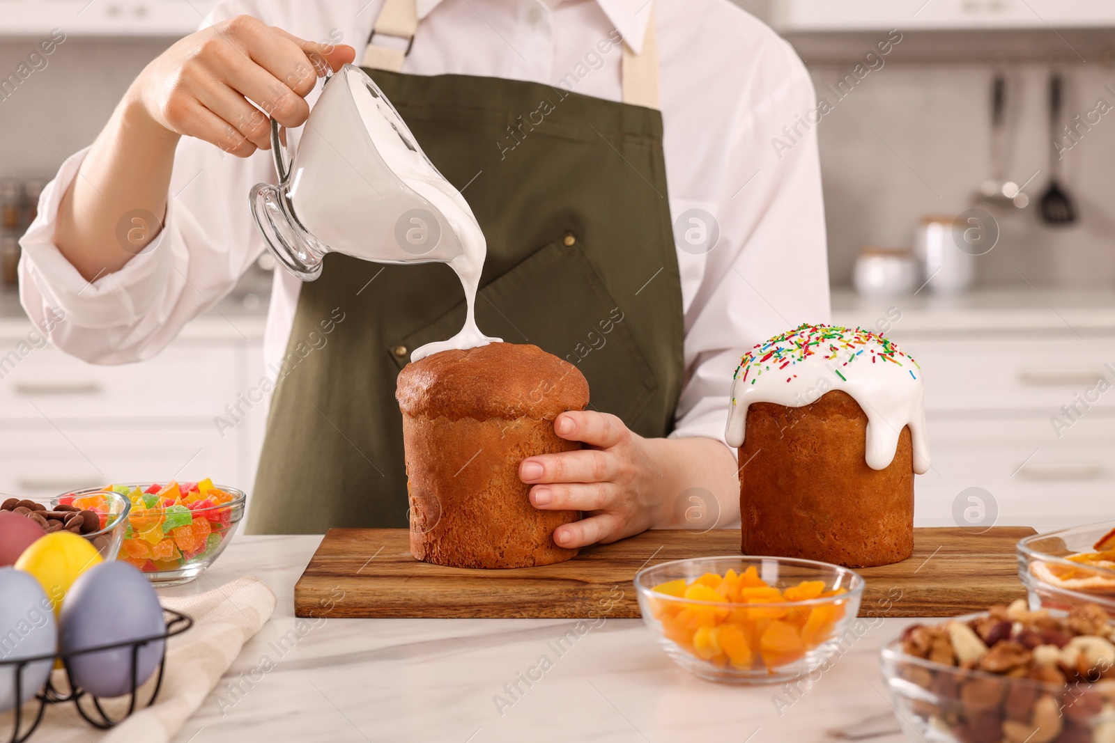 Photo of Woman decorating traditional Easter cake with glaze at white marble table in kitchen, closeup