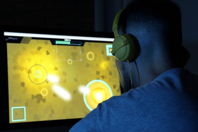 Photo of Man with headphones playing video game on modern computer in dark room