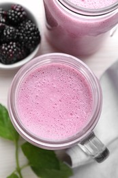 Photo of Mason jar of blackberry smoothie and berries on white table, flat lay