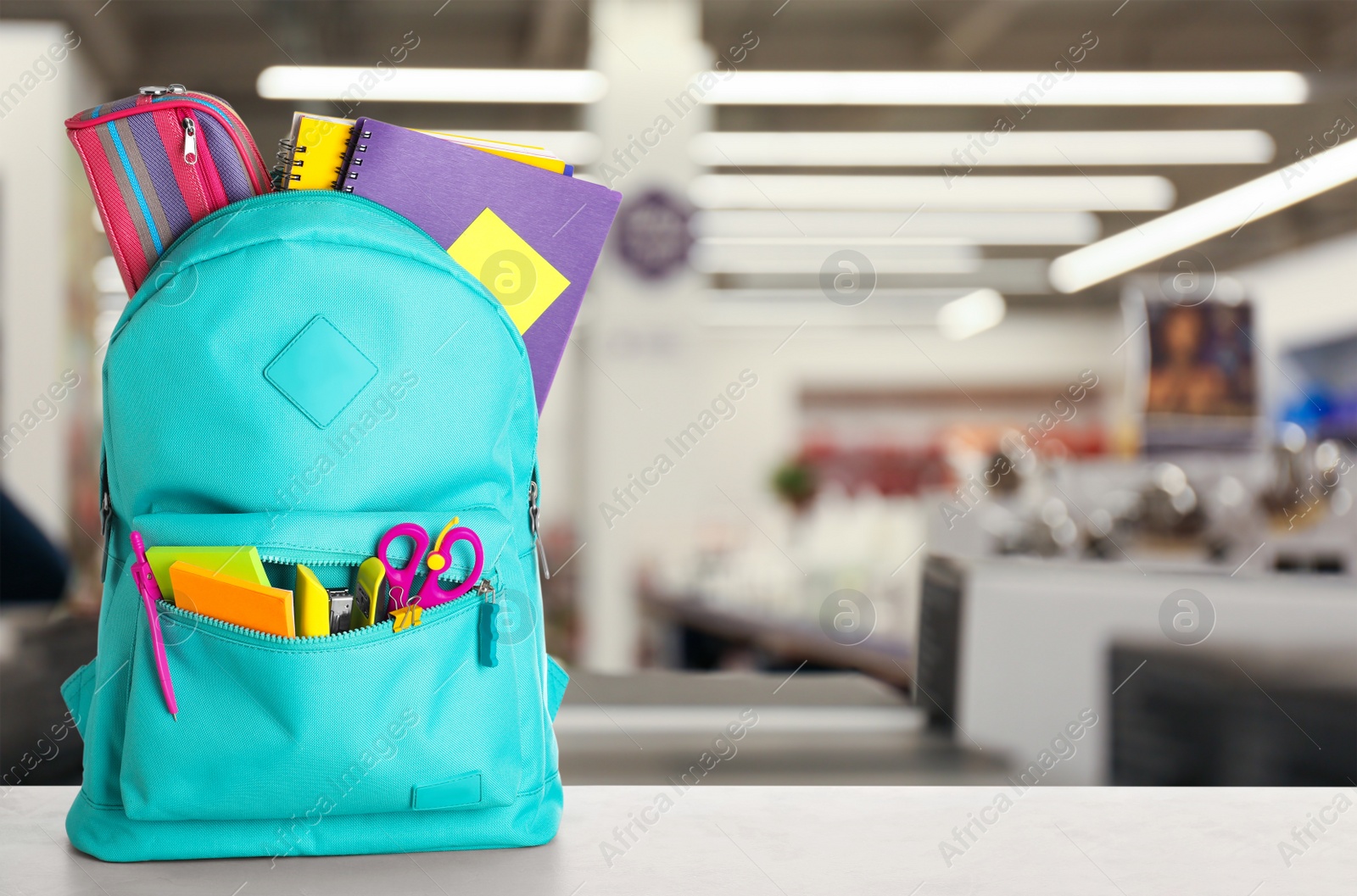 Image of Bright backpack with school stationery on table in shopping mall. Space for text