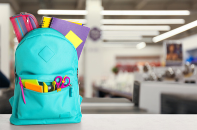 Image of Bright backpack with school stationery on table in shopping mall. Space for text