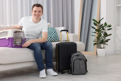 Photo of Travel with pet. Man near carrier with cat on sofa at home
