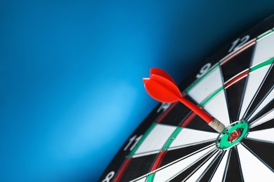 Photo of Red arrow hitting target on dart board against blue background. Space for text