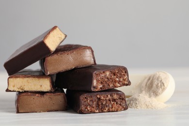 Photo of Pieces of tasty bars and spoon with protein powder on white table
