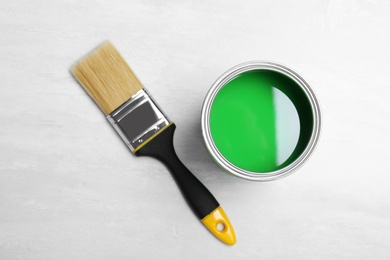 Photo of Can with green paint and brush on light background, top view