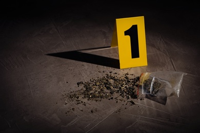 Photo of Scattered cannabis and crime scene marker on grey stone table. Space for text