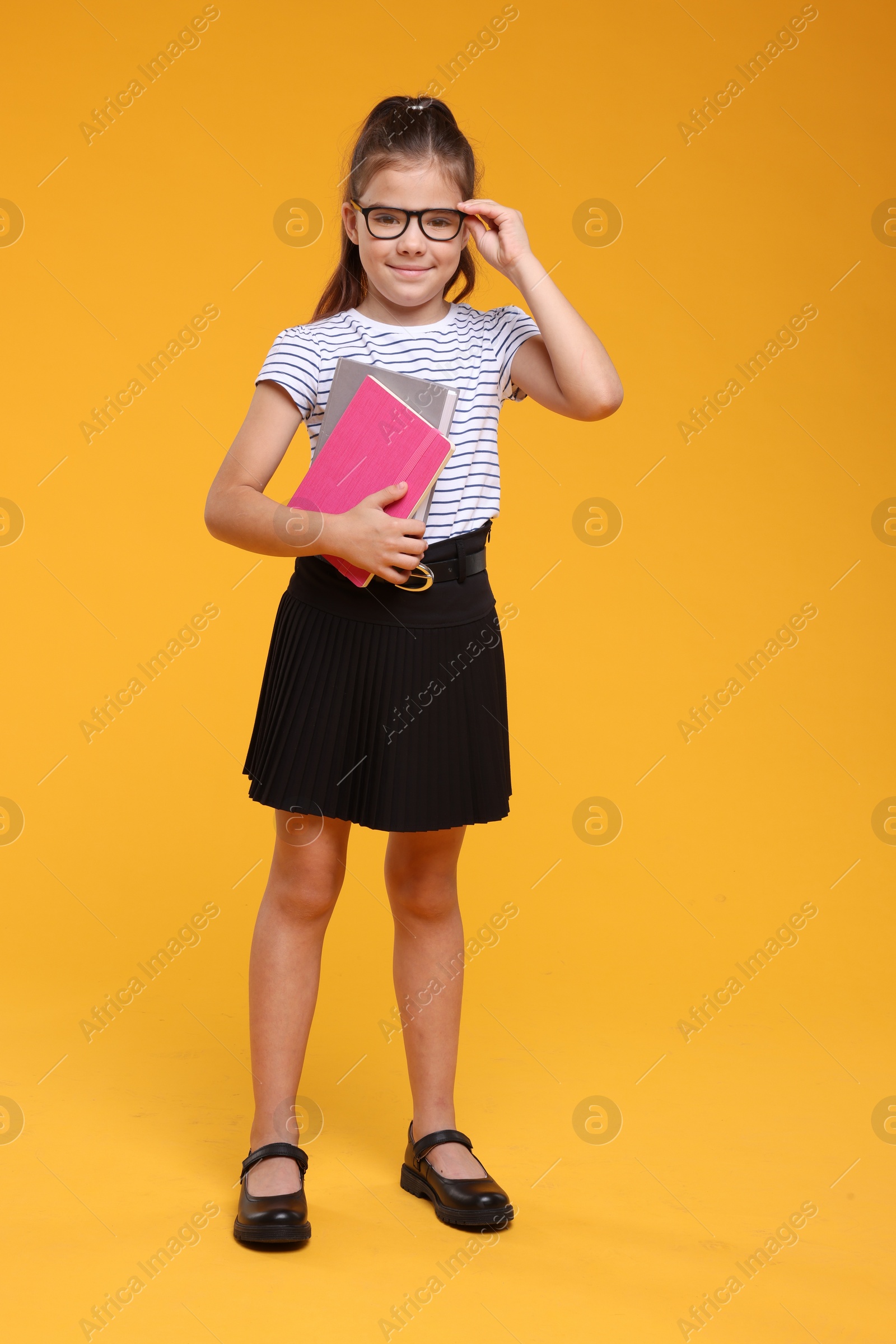 Photo of Cute schoolgirl in glasses with books on orange background