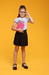 Cute schoolgirl in glasses with books on orange background