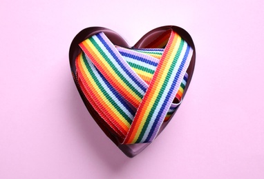 Photo of Heart shaped mold with bright rainbow ribbon on color background, top view. Symbol of gay community