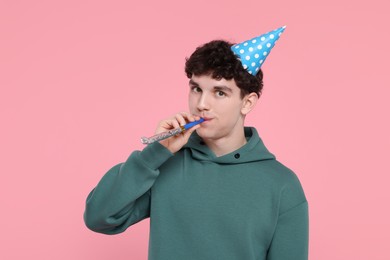 Young man in party hat with blower on pink background