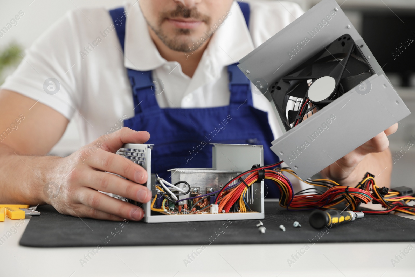 Photo of Male technician repairing power supply unit at table, closeup