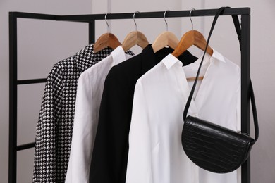 Photo of Rack with stylish women's clothes and bag near light wall
