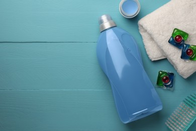 Photo of Bottle of fabric softener, laundry capsules and towel on light blue wooden table, flat lay. Space for text