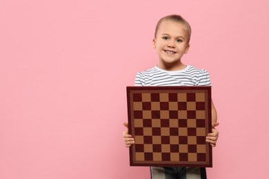 Photo of Cute girl holding chessboard on pink background. Space for text