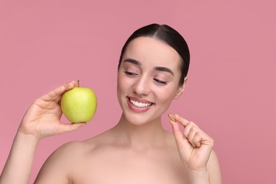 Beautiful young woman with vitamin pill and apple on pink background