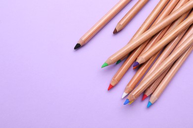 Photo of Many colorful pastel pencils on violet background, flat lay and space for text. Drawing supplies